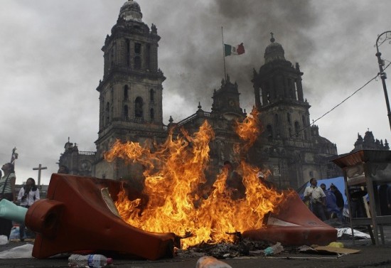 Teachers and protesters stand near a burning barricade before they are evicted from Zocalo Square by the riot police in Mexico City. Courtesy of International Business Times for TTD